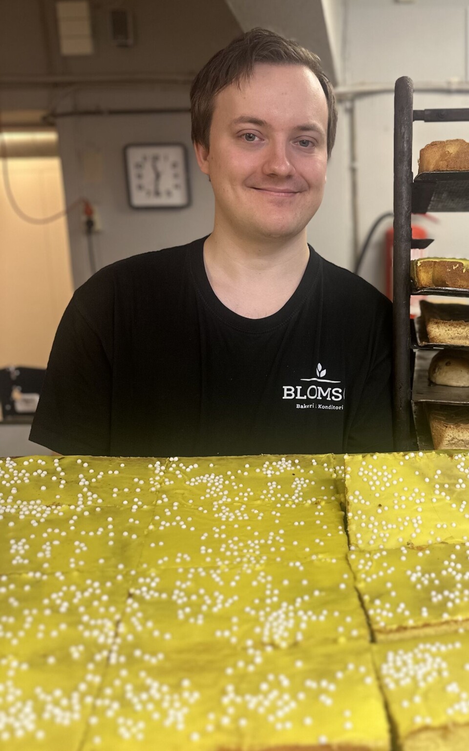 Fredrik Pedersen hadde sitt fulle hyre med å bake på jubuelimsdagen. Mann i svart t-skjorte holder en stor formkake med gul glasur.