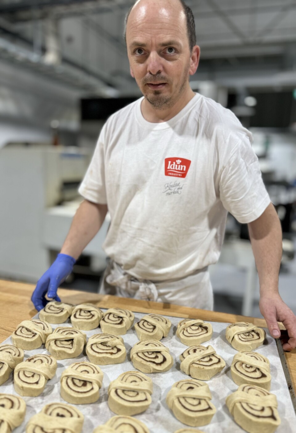 Arne Raymond Kristensen har sammen med de andre ansatte hatt travle dager i oppstarten av det nye bakeriet. Baker som holder i et brett med ustekte kanelsnurrer.