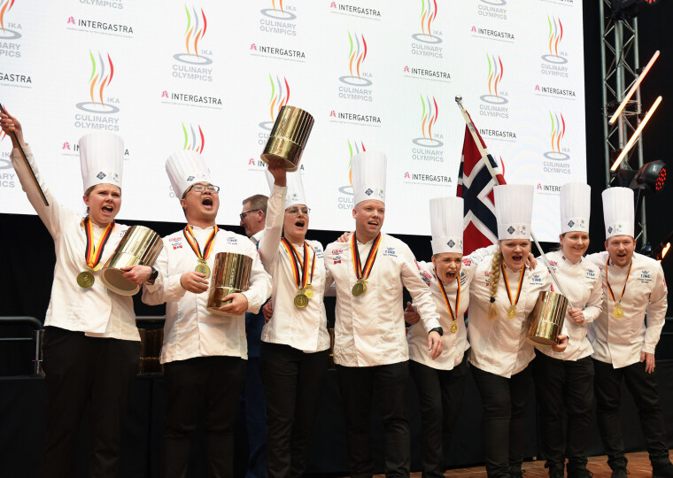 De Norske Kokkelandslagene Community Catering fikk en historisk bronse i Kokke-OL 2024. Åtte kokker med kokkekatter med pokaler og norsk flagg som jubler.