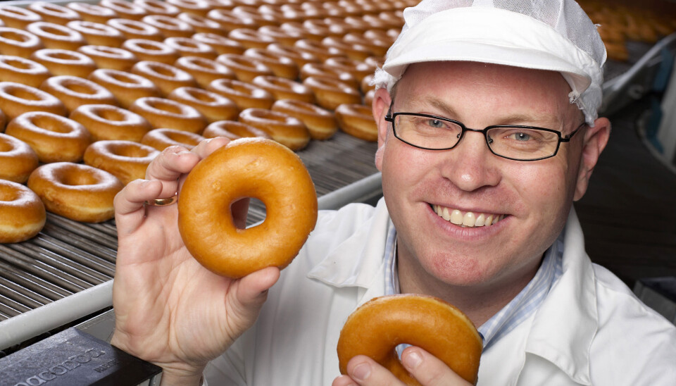 Bernt Ove Søvik og Millba kan glede seg over stor interesse for bedriftens ti nye stillinger. Mann med briller som holder to donuts foran en produksjonslinje full av donuts.