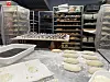 Deigemner ligger på melet bakebord foran hyller fulle av brød i et profesjonelt bakeri.