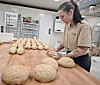 Baker former brøddeig på trebord foran rekker av deigemner i bakeri