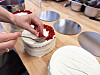 Hender som pynter en hvit kake med røde smuler på et bakerkjøkken