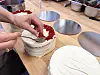 Hender som pynter en hvit kake med røde smuler på et bakerkjøkken