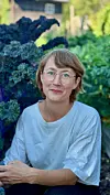 Person med briller sitter i grønnsakshage omgitt av grønnkål