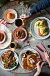 Overhead-bilde av et bord med ulike frokost- og lunsjretter, kaffe, drikke og hender som dekker opp.