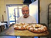 En mann holder to nybakte brød på et bord i et enkelt arbeidsrom.