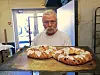 En mann holder to nybakte brød på et bord i et enkelt arbeidsrom.