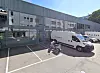 Hvit varebil parkert foran et moderne næringsbygg med store vinduer og tomme parkeringsplasser.