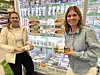 To kvinner holder Bakehuset-produkter foran en butikkhylle med brød og kampanjeplakater i Kiwi.