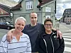 Tre personer står arm i arm utenfor Jenseg Bakeri og Konditori i en gate.