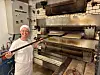 Anne-Berit Randen skyver rullekaker inn i en stor gammel steinovn i et bakeri.