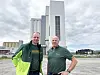 To menn står foran en høy bygning med grå fasade under overskyet himmel.