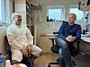 To menn sitter i et bakerirom med arbeidsbenk, vindu og utstyr i bakgrunnen.