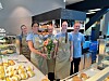 Fem ansatte står ved en disk med bakverk og blomster i en moderne kafé.