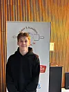 Ung mann i svart hettegenser står foran et skilt med bakeri- og konditoritekst.
