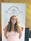 Ung jente står foran et banner med baker- og konditorlogo i et innendørs rom.