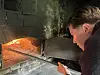 Person ser inn i en steinovn med synlige flammer og et brett med brød.