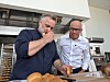 To menn står ved en kjøkkenbenk og gjør klart mat i et lyst kjøkken.