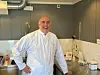 Person i hvit arbeidsdrakt står ved en benk i et moderne kjøkken- eller laboratorierom.