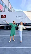 To kvinner står foran en Idun Bakeri-lastebil og holder armene ut på en parkeringsplass.