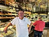 En mann står foran glassmontre med bakervarer i en konditori, med en kunde i rødt i bakgrunnen.
