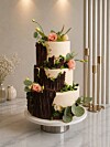 Fleretasjes kake med blomster og blader på et fat i et lyst rom.