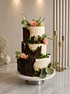 Fleretasjes kake med blomster og blader på et fat i et lyst rom.