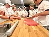 Personer i hvite klær samles rundt en benk og jobber med deig hos Idun Industri.