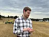 En mann i rutet skjorte står i en kornåker med maskiner i bakgrunnen.
