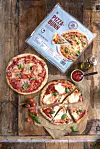 To pizzaer, en pizzaboks, tomatsaus og små tomater på et trebord.