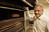 Baker åpner en stor industriovn med brød inni.