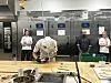 Baker arbeider ved en benk i et storkjøkken, omgitt av to kolleger og rustfrie apparater.