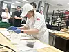 Baker i hvit uniform tilbereder mat ved en arbeidsbenk i et profesjonelt kjøkken.