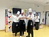 Kokker i uniform poserer med trofeer og medaljer foran en arrangementsvegg.