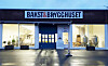 Opplyst fasade med skiltet Bakst & Brygghuset, butikkvinduer og våt brostein.