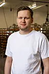 Portrett av en mann i hvit T-skjorte foran hyller i et produksjonslokale.