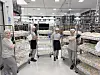 Fire ansatte i grå arbeidsklær og hårnett står mellom vogner og reoler i et lyst industrilokale.