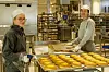 To bakere står ved brett med gyllenbrune bakervarer i et industribakeri.