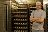 Baker med armene i kors foran hyller med brød og bakverk.