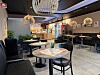 Moderne kaféinteriør med runde bord, stoler, planter og hengende lamper.