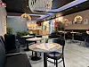 Moderne kaféinteriør med runde bord, stoler, planter og hengende lamper.