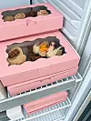 Åpne rosa esker med assorterte bakervarer i en kjølt butikkmonter.