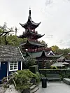 Asiatisk pagode omgitt av grøntområder, benker og bygninger i Tivoli i København.