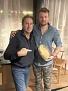 To menn poserer innendørs, mens den ene holder et rundt, gullfarget objekt.