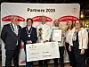 Gruppe poserer med stor sjekk og innrammet dokument foran en sponsorvegg.