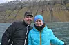 To personer i friluftsklær smiler foran et fjellvann med bratte fjell i bakgrunnen.