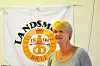 Kvinne med kort blondt hår foran et hvitt banner med jubileumslogo.