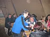 Gruppe mennesker samles rundt et bord, mens en mann i blå jakke bøyer seg frem.