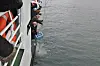 Personer arbeider ved siden av et fartøy over gråblått vann.